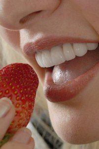 Lady with amazing smile due to dental veneers biting into strawberry.