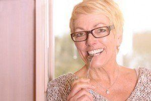 Close up Happy Middle Age Blond Woman, Wearing Eyeglasses, Biting a Fork While Looking at the Camera.