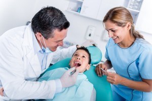 Pediatric dentist looking into boy's mouth with mother beside him.